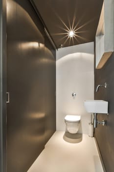 a bathroom with a toilet, sink and mirror on the wall in it's right corner there is a light coming from above