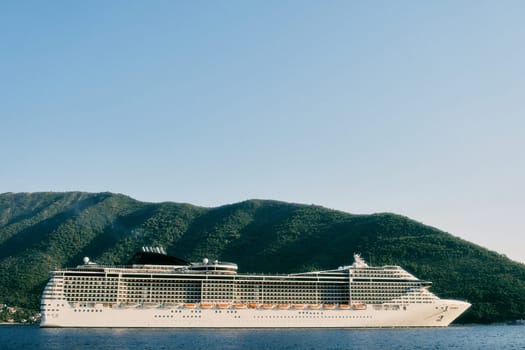 Huge white cruise ship sails on the sea past a green mountain. High quality photo