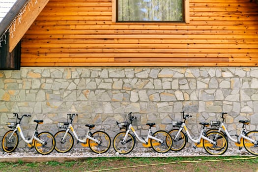 Row of colorful two-wheeled bicycles with baskets stands against the wall of a house. High quality photo