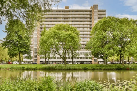 an apartment building with trees and water in the fore - image is taken from across the pond to the buildings