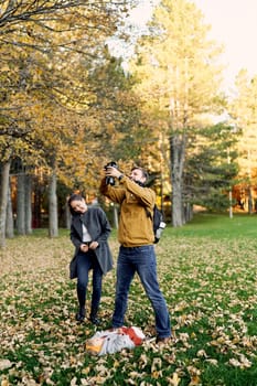 Dad takes a picture of a little girl lying on fallen leaves on the lawn standing next to mom. High quality photo