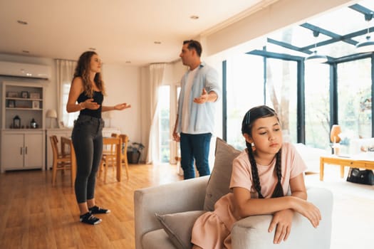 Annoyed and unhappy young girl sitting on sofa trapped in middle of tension by her parent argument in living room. Unhealthy domestic lifestyle and traumatic childhood develop to depression.Synchronos