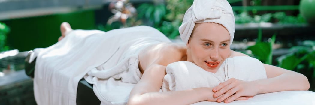 Beautiful young woman relaxes on a spa bed surrounded by nature. ready for a body massage. Attractive female in white towel lying peacefully during waiting for body massage. Close up. Tranquility