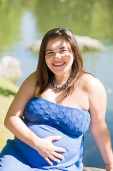 portrait of a happy pregnant woman in a bright blue dress and fanning herself with a red fan, sitting on a bench in a park by the lake, desired pregnancy,High quality photo