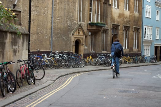 Solitary cyclist on a street with bicycles lined up against a wall in Oxford, England, UK.