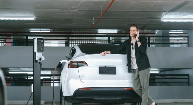 Young man travel with EV electric car to shopping center parking lot charging in downtown city showing urban sustainability lifestyle by green clean rechargeable energy of electric vehicle innards