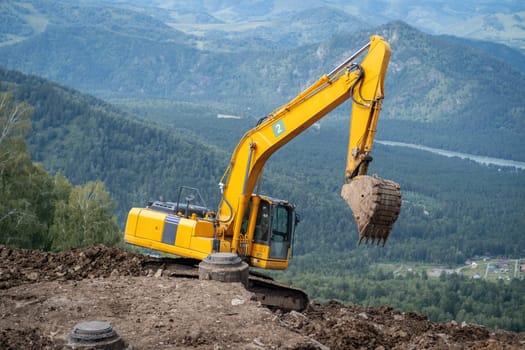 A yellow excavator works in the mountains. Construction of roads and houses in beautiful mountains.