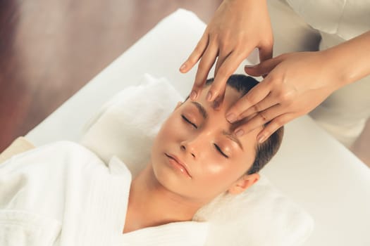 Caucasian woman enjoying relaxing anti-stress head massage and pampering facial beauty skin recreation leisure in dayspa modern light ambient at luxury resort or hotel spa salon. Quiescent