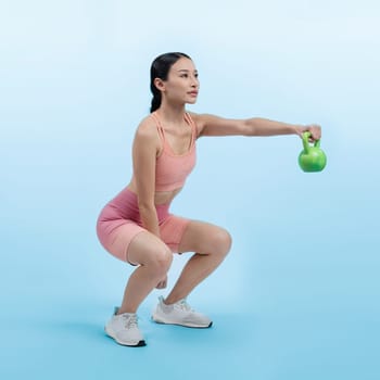 Vigorous energetic woman doing kettlebell weight lifting exercise on isolated background. Young athletic asian woman strength and endurance training session as body workout routine.