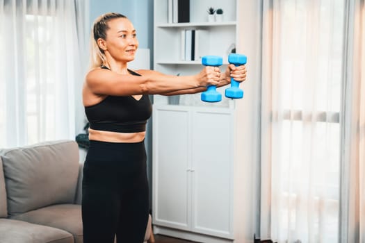 Athletic and sporty senior woman engaging in body workout routine with lifting dumbbell at home as concept of healthy fit body with body weight lifestyle after retirement. Clout