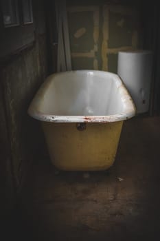 One old and dirty vintage bathtub is located during the day in a dark bathroom of an abandoned house, close-up side view.