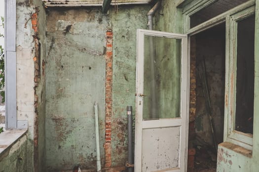 Old, dirty doors with windows and a shabby green wall in an old abandoned house, close-up side view. Concept of home renovation, interior abandoned houses.