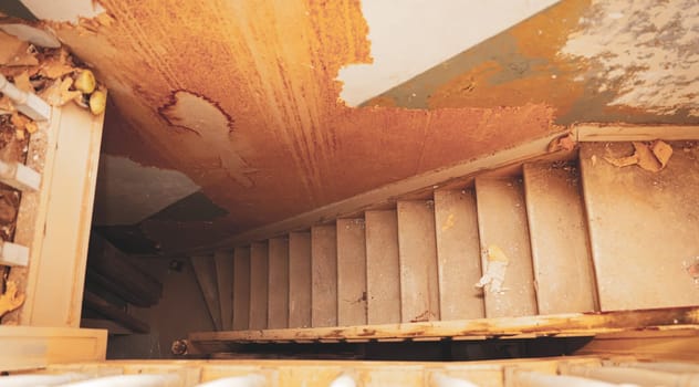 One old, dirty staircase leading down and shabby walls in an old abandoned house, close-up side view. Home renovation concept, abandoned house interiors.