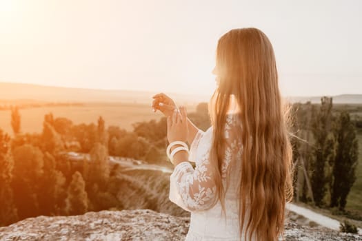 Romantic beautiful bride in white dress posing with sea and mountains in background. Stylish bride standing back on beautiful landscape of sea and mountains on sunset