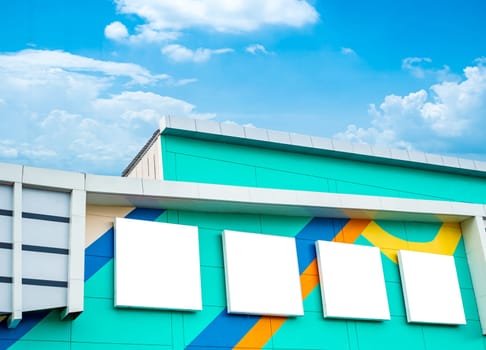 Green building with white blank sign on the background of blue sky and white clouds.