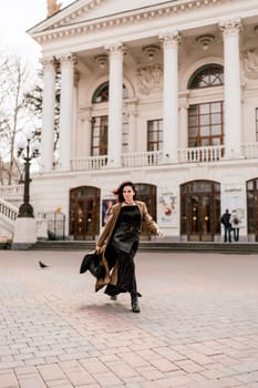 Woman street lifestyle. Image of stylish woman walking through European city on sunny day. Pretty woman with dark flowing hair, dressed in a beige raincoat and black, walks along the building