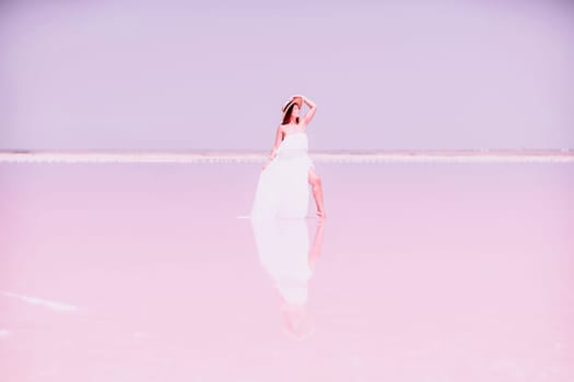 Woman in pink salt lake. She in a white dress and hat enjoys the scenic view of a pink salt lake as she walks along the white, salty shore, creating a lasting memory