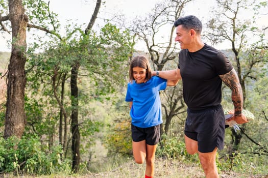 father and daughter stretching and warming up for sports in the countryside, concept of sport with kids in nature and active lifestyle, copy space for text