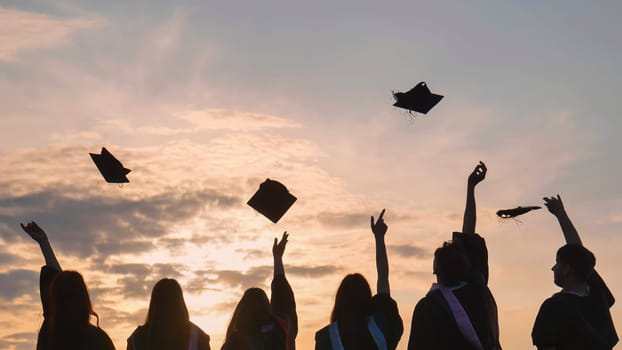 Student graduates toss their caps at sunset