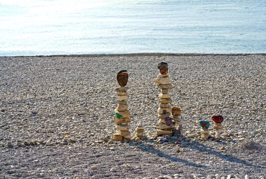 figures made of stones on the beach against the backdrop of the sea. A vertical figure made of stones stands against the backdrop of water.