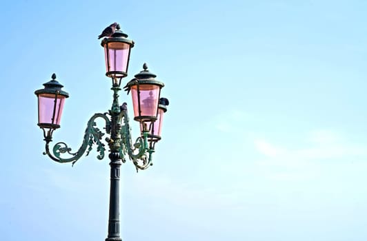 Lantern on the street of Venice. The famous pink lights of Venice. Four lamps with pink glass are on an ornate black metal lamp post.