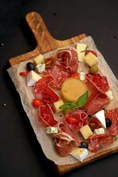 cold cuts - jamon, ham, salami on a wooden board on a black background