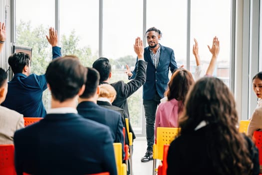 In a boardroom strategy session businesspeople participate in a meeting and seminar. Hands raised to ask questions demonstrate the collaborative nature of this planning workshop.