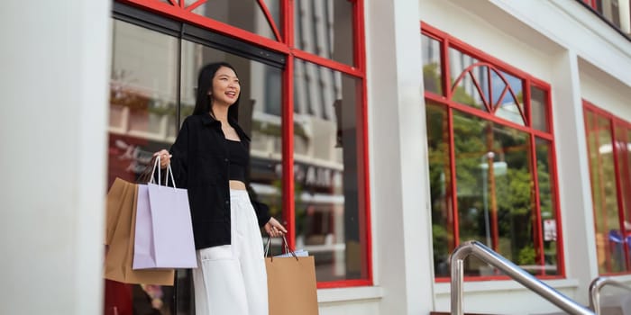 Happy beautiful young stylish woman with shopping bag while walking come out of mall on holiday Black Friday.