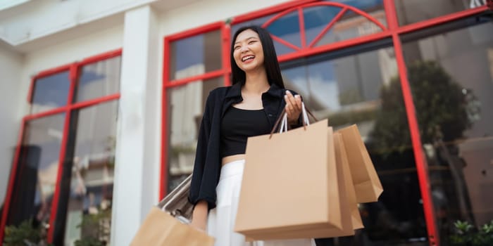 Happy beautiful young stylish woman with shopping bag while walking come out of mall on holiday Black Friday.