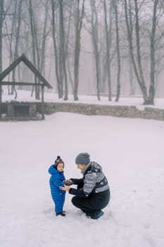 Mom puts on mittens to a little girl squatting in a snowy forest. High quality photo