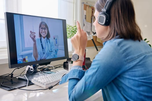 Video call conference with doctor, young female in headphones sitting at home talking to therapist, using computer, getting online medical consultation. Medicine, service, technology, people concept