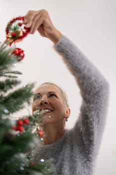 Cheerful elderly woman decorat the christmas tree. Christmas atmosphere at cozy home interior.