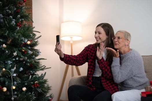 Cheerful daughter and mother celebrating christmas at home and with friend and family through a video call.