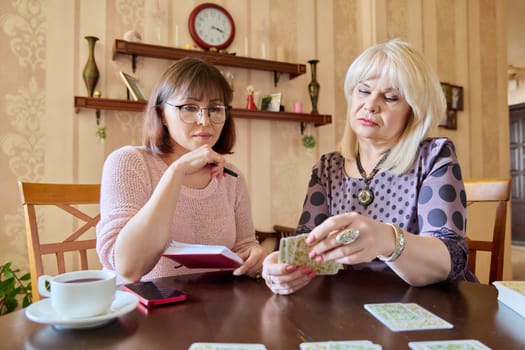 Two middle aged women laying out cards at home on the table. Game, psychology, metaphorical associative cards, esotericism prediction, communication lifestyle friendship of mature women