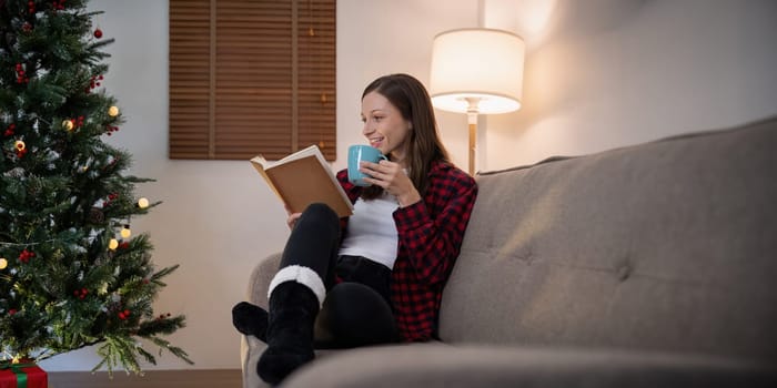Young cute woman holding cup coffee or tea and read interest book. Concept of Christmas atmosphere at home.