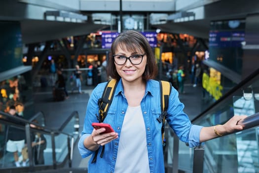 Woman on escalator stairs in building of city transport station with smartphone. Female using fast internet connection network for online ticketing service mobile application timetable transport route