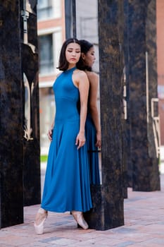 Beautiful asian ballerina in blue dress and pointe shoes posing outdoors. Vertical photo