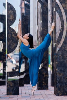 Beautiful asian ballerina in blue dress and pointe shoes posing outdoors. Vertical photo