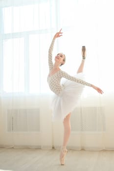 Beautiful ballerina in body and white tutu is training in a dance class. Young flexible dancer posing in pointe shoes