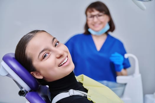 Young teenage female at dental examination treatment checkup in clinic. Teen girl sitting in chair doctor dentist with tools examining patient teeth. Adolescence hygiene dentistry dental health care