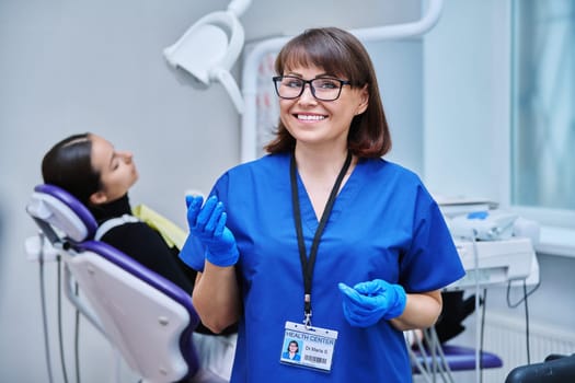 Portrait of smiling female dentist looking at camera with young girl patient sitting in dental chair. Visit to dentist examination treatment. Dentistry hygiene dental teeth health care concept