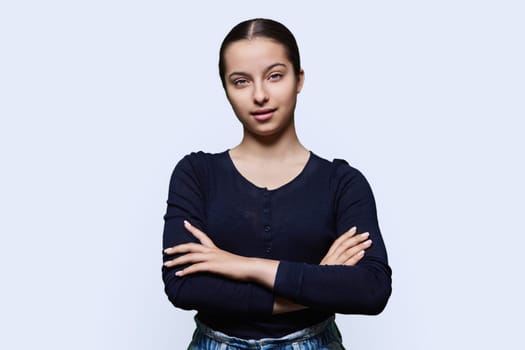Portrait of teenage smiling female looking at camera on white studio background. Confident teen girl with crossed arms. Adolescence, high school, youth 15, 16 years old concept
