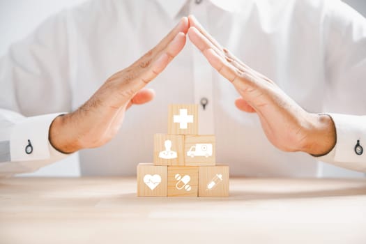 Symbolic representation of healthcare and insurance through a doctor hand on a wooden cube block with protection sign. Stacked medical icons showcase comprehensive medical care. Health care concept
