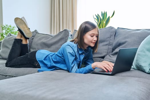Young woman lying on sofa using laptop. Internet technologies for study leisure, female freelancer working remotely, university student watching online course, rest communication in social networks