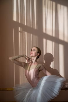 Beautiful graceful ballerina is practicing in the hall against the background of a window. Slender woman in tutu and pointe shoes in a dance class