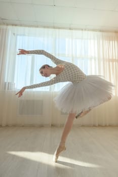 Beautiful ballerina in body and white tutu is training in a dance class. Young flexible dancer posing in pointe shoes