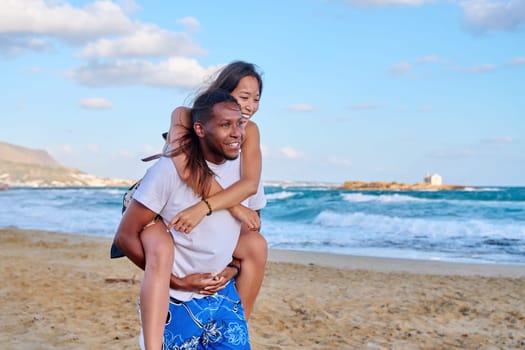 Happy young beautiful couple having fun on beach, copy space. Afro american asian couple laughing enjoying vacation in seaside nature. Multicultural, multiethnic family, relationships, togetherness