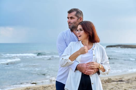 Outdoor portrait of mature couple hugging on beach, background of sea nature, copy space. Middle-aged happy romantic man and woman. Relationships, feelings, lifestyle, marriage, family, people concept