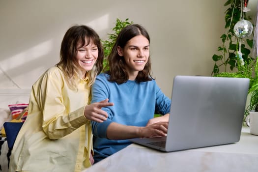 Teenage friends male and female using laptop at home for leisure. Youth, lifestyle, communication, friendship, technology, young people concept