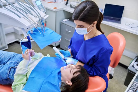 Doctor dentist treats teeth to a young teenage female patient. Real process of treatment, dental care, orthodontics, therapy, health care, dentistry concept